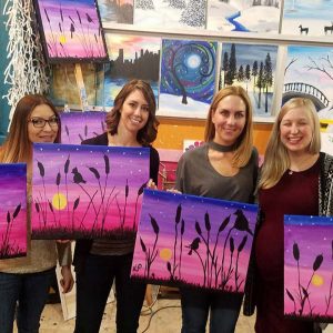 four women holding up their completed paintings at a paint & sip adult party