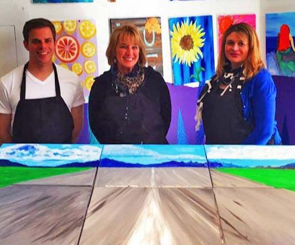 three employees wearing aprons at a paint & sip team building event