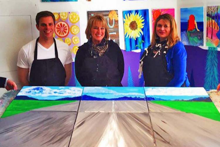 three employees wearing aprons at a paint & sip team building event